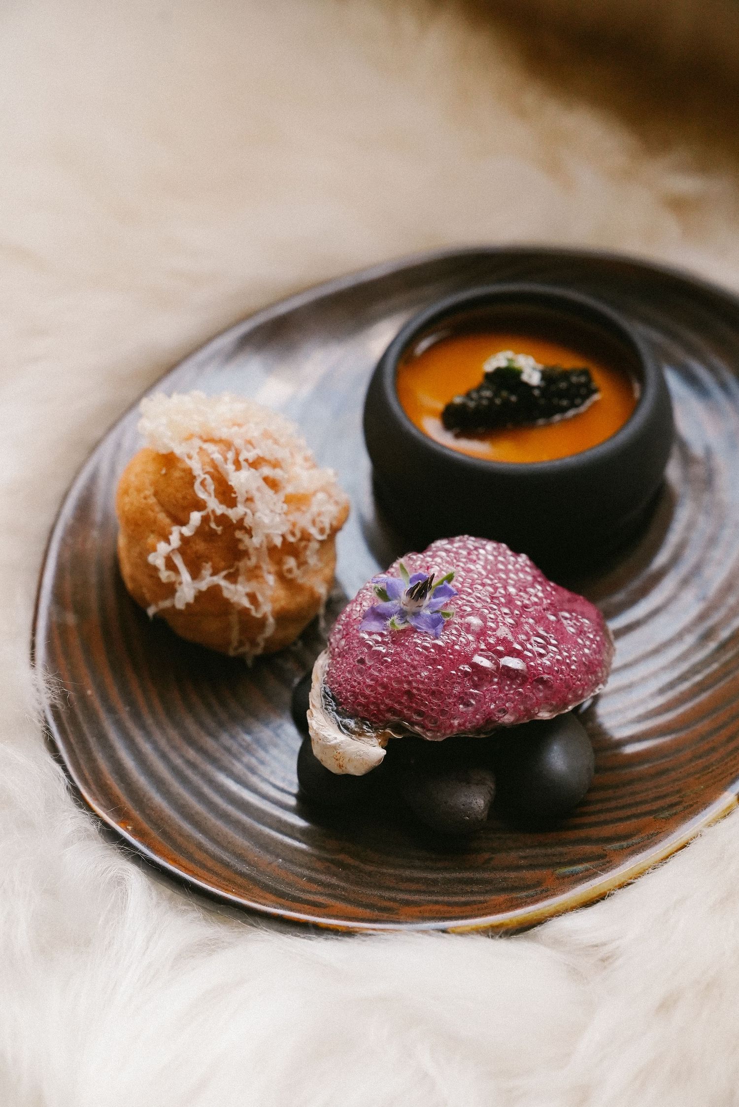 Artisan plated dessert with three components including caviar and berry mousse on dark plate.