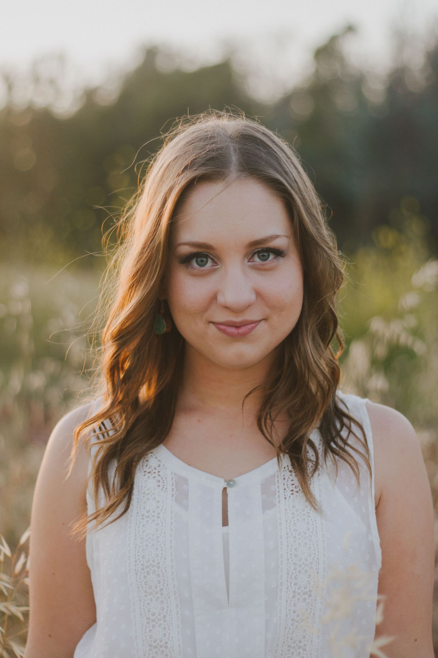 Young woman with wavy auburn hair smiling softly in golden sunlit meadow.