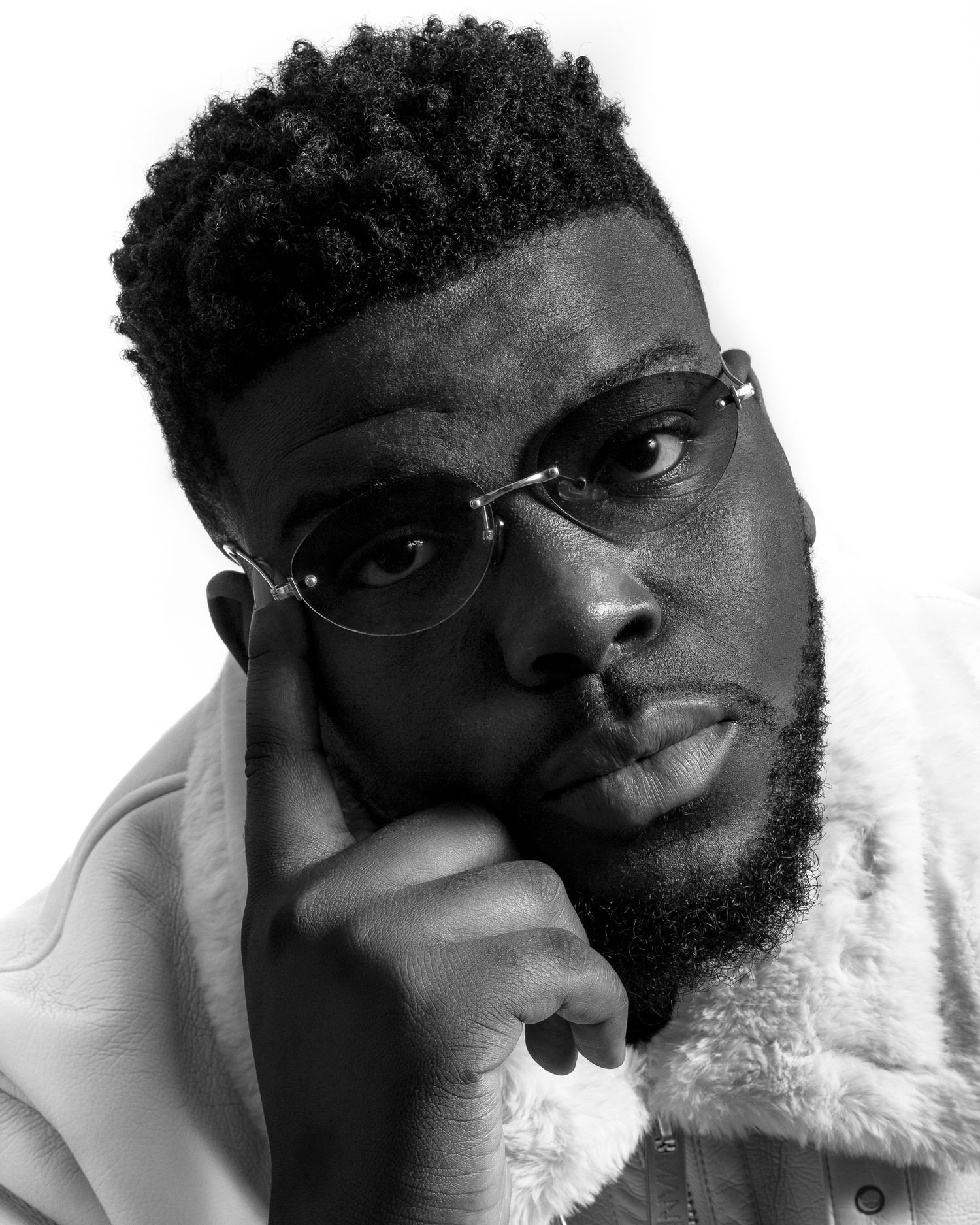 Black and white portrait of a young man with glasses and a beard, resting his chin on his hand thoughtfully.