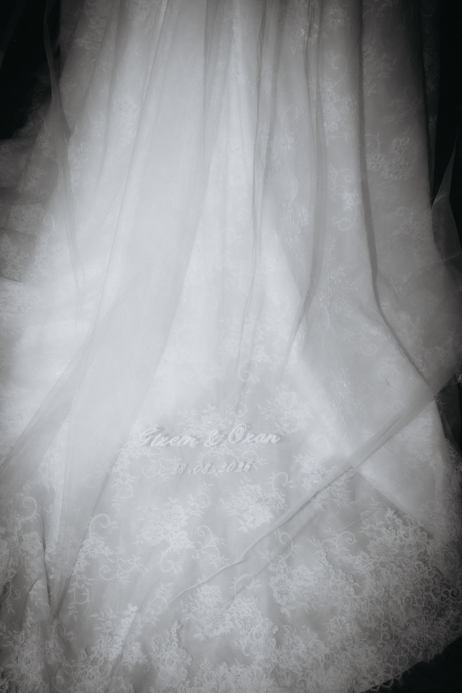 Close-up black and white photo of an elegant wedding dress with delicate lace details and flowing sheer fabric layers.