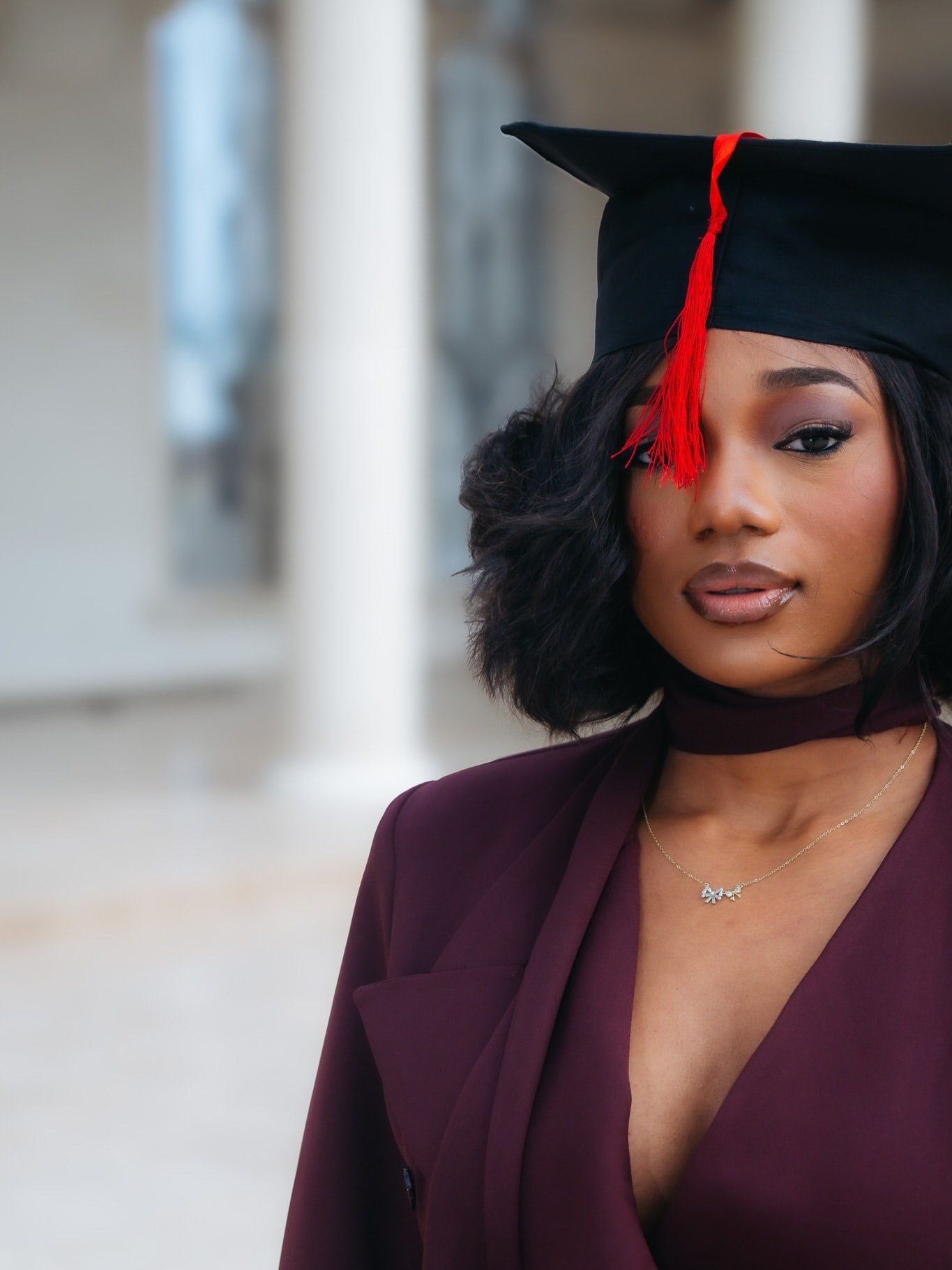 Close-up portrait of young woman wearing black graduation cap with red tassel and deep-V maroon blazer.