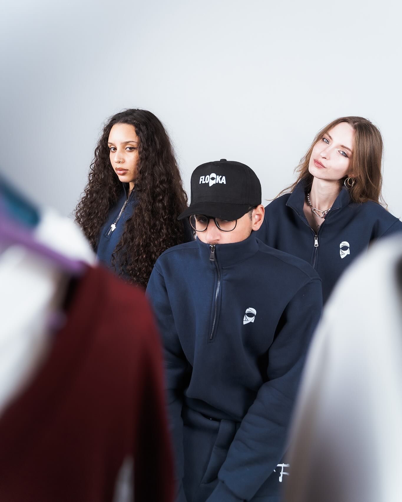 Three models in navy blue streetwear stand among clothing racks in a studio.