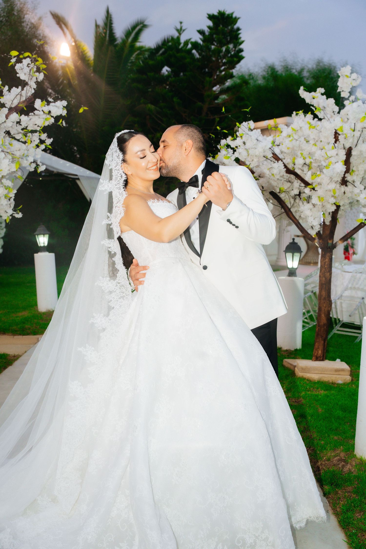 Bride and groom share a romantic kiss during outdoor wedding ceremony, bride in elegant ball gown with veil.