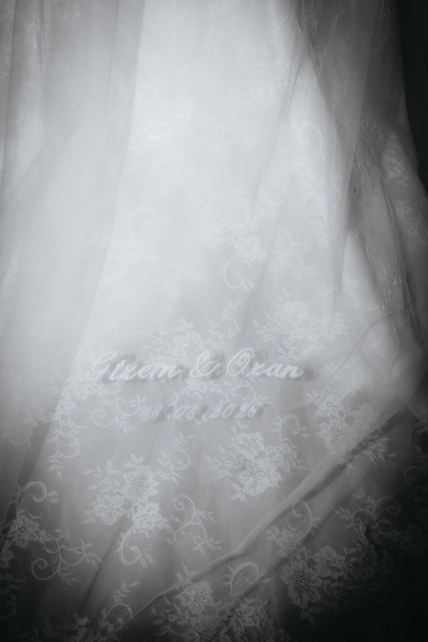 Black and white photo of a lace wedding veil with embroidered text reading Neon and Ozan with a date.