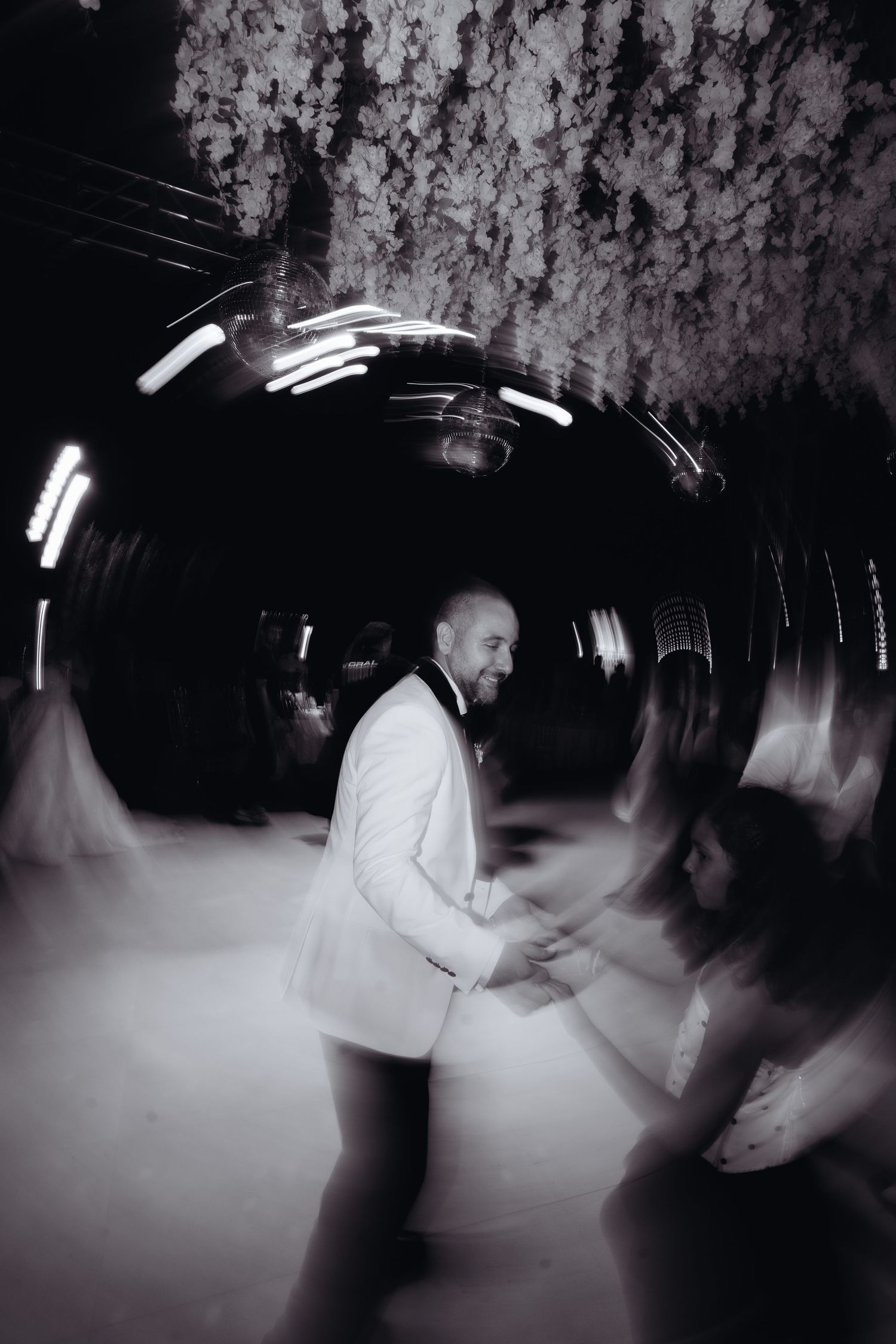 Black and white photo of a groom in white suit dancing at wedding reception with motion blur effect.
