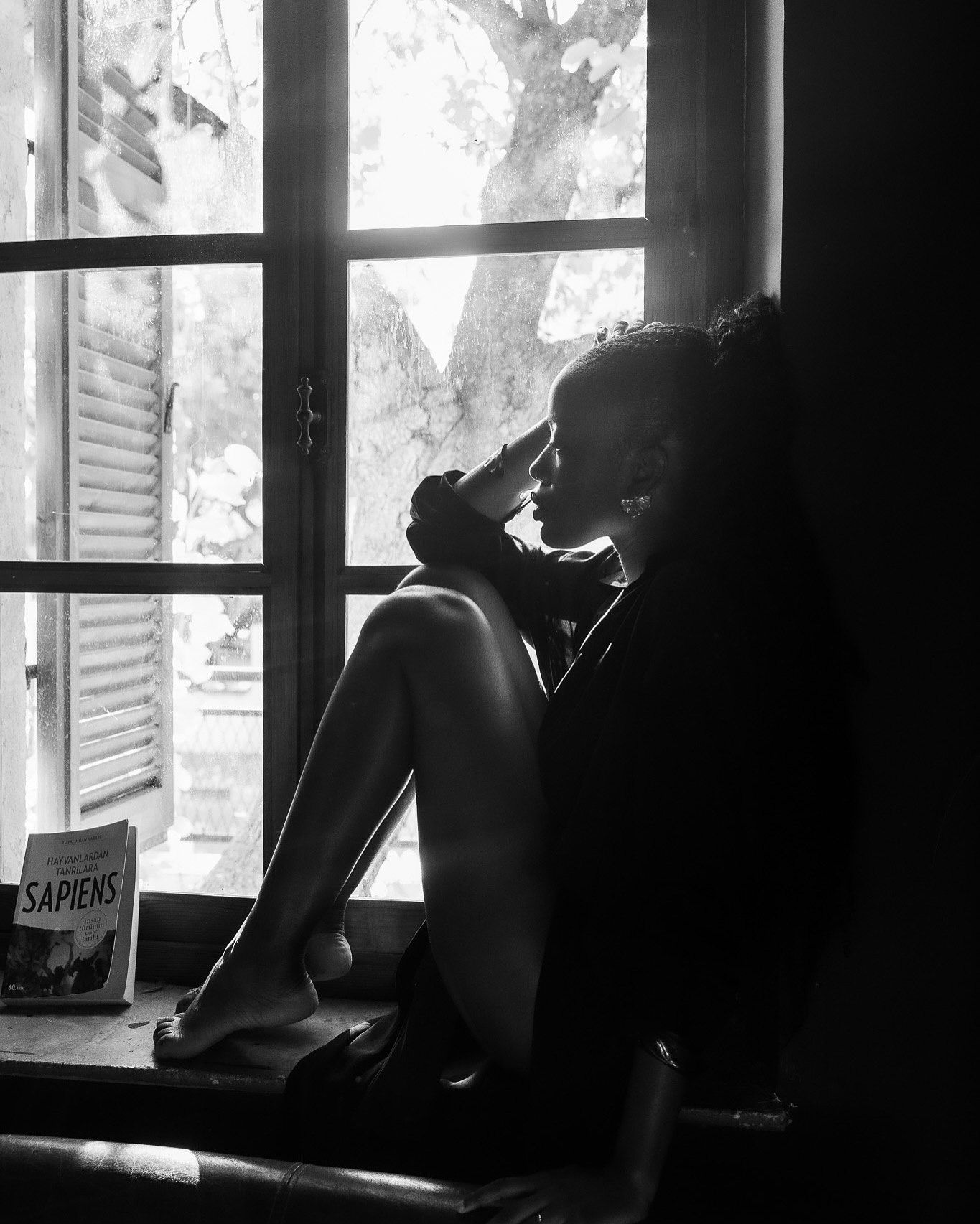 Black and white photo of a person sitting by a sunlit window with a Sapiens book nearby.