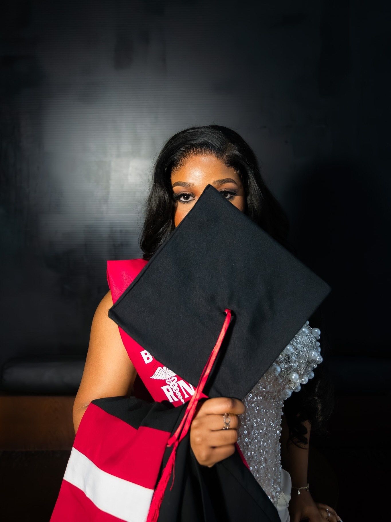Graduate hiding face behind black mortarboard cap wearing red BSN sash.