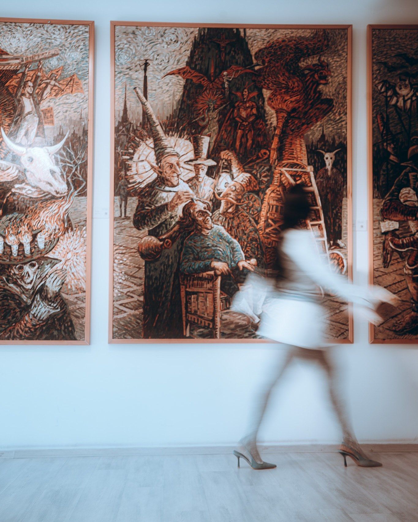 Blurred woman in white dress walks past large ornate paintings in a contemporary art gallery.