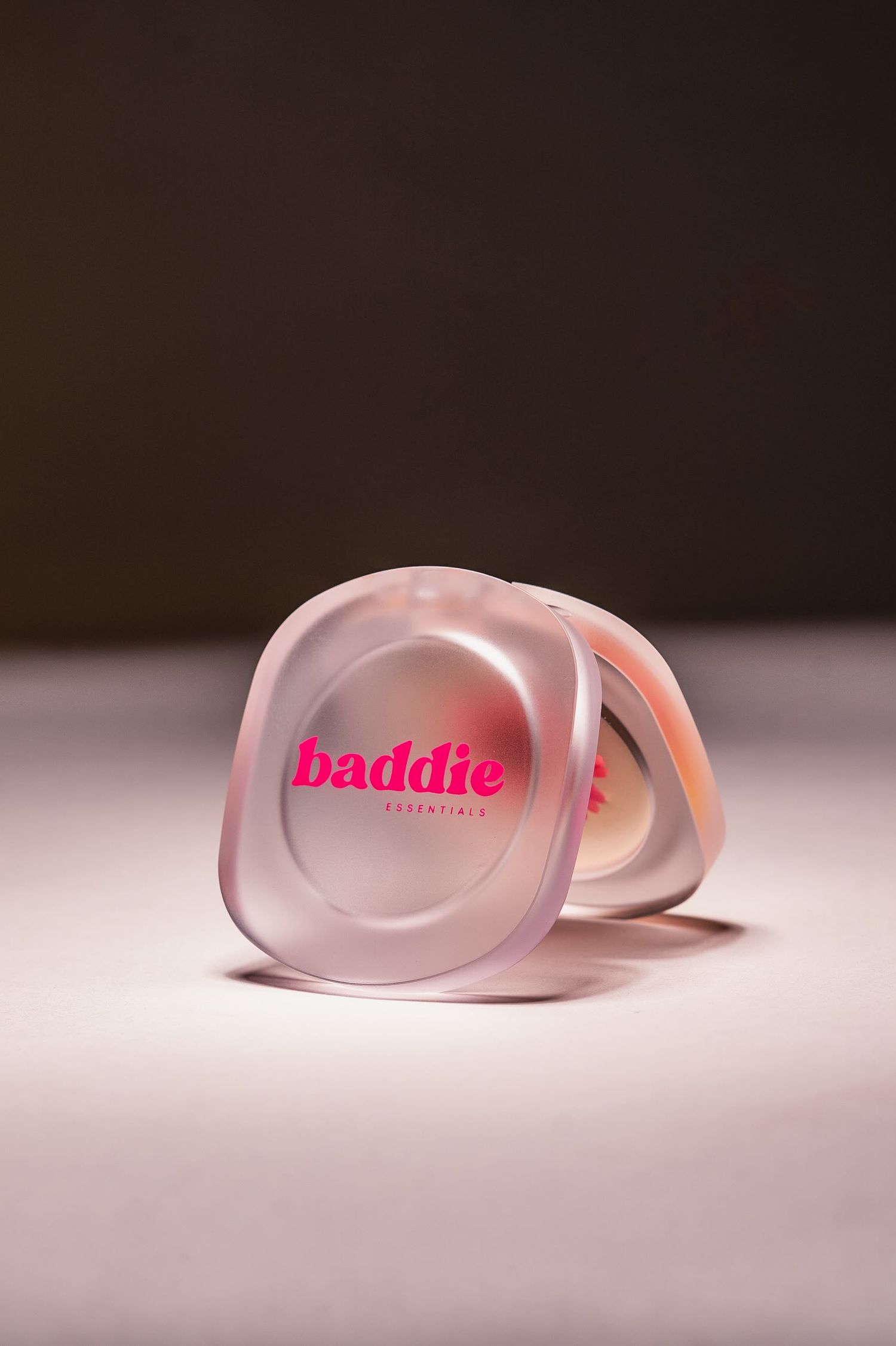 Baddie Essentials pink translucent compact makeup container on a soft lit surface.
