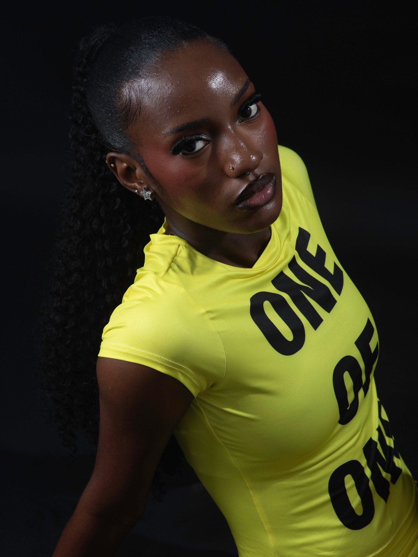 Woman in yellow athletic shirt with ONE DE ON print, dark background, fitness wear photo.