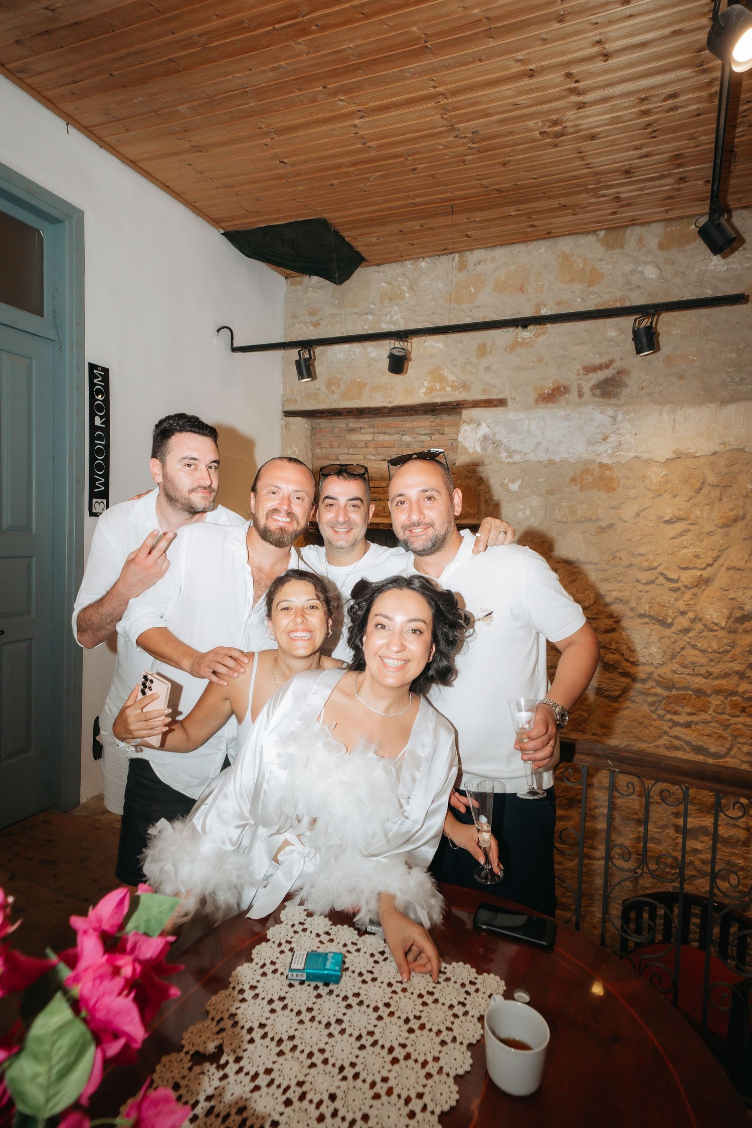 Group of friends posing together at a wedding celebration in a rustic stone-walled venue.
