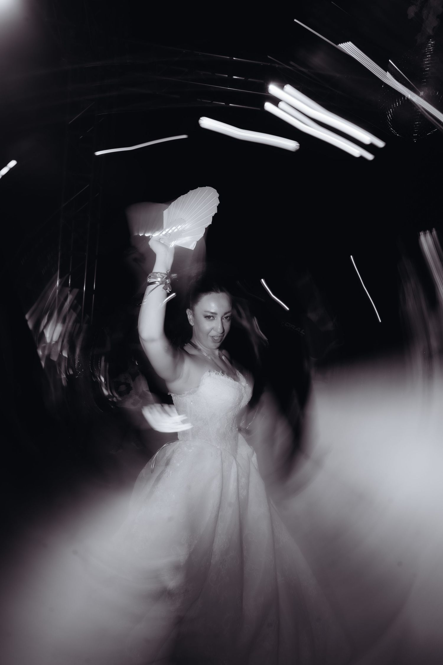 Black and white photo of a bride in a white gown dancing with motion blur and light streaks at a wedding reception.