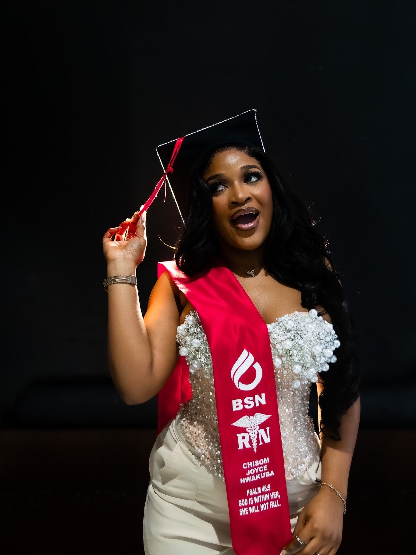 Black woman in BSN RN graduation sash and cap celebrating at ceremony.