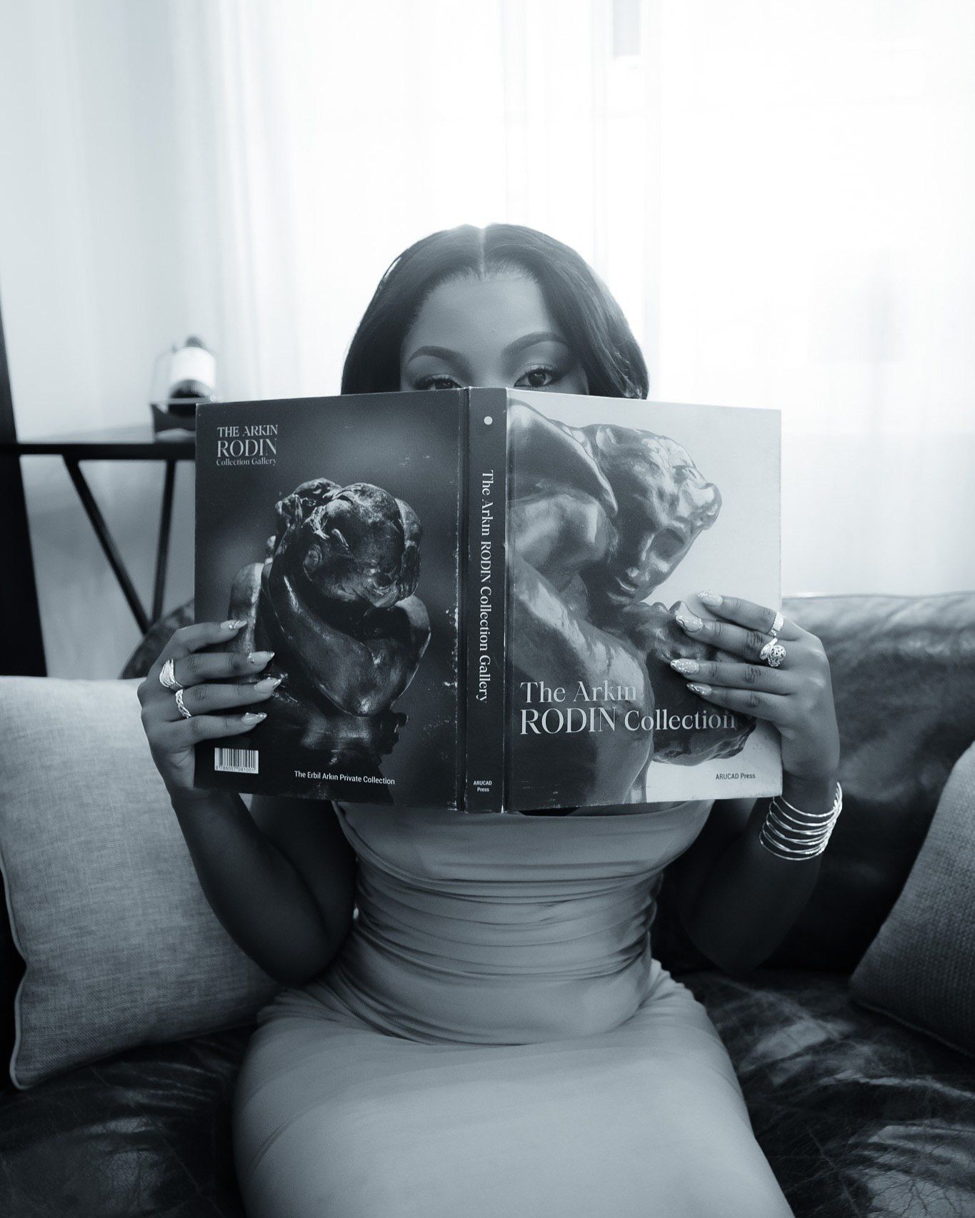 Woman reading The Ark Rodin Collection art book on a couch in black and white photo.