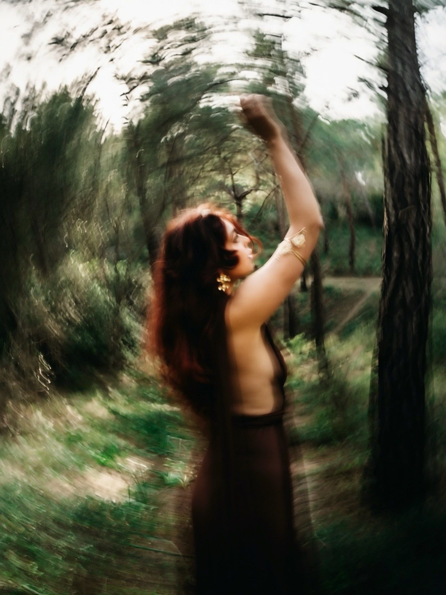 Blurred artistic photo of a woman in a dark dress dancing among trees in a forest.