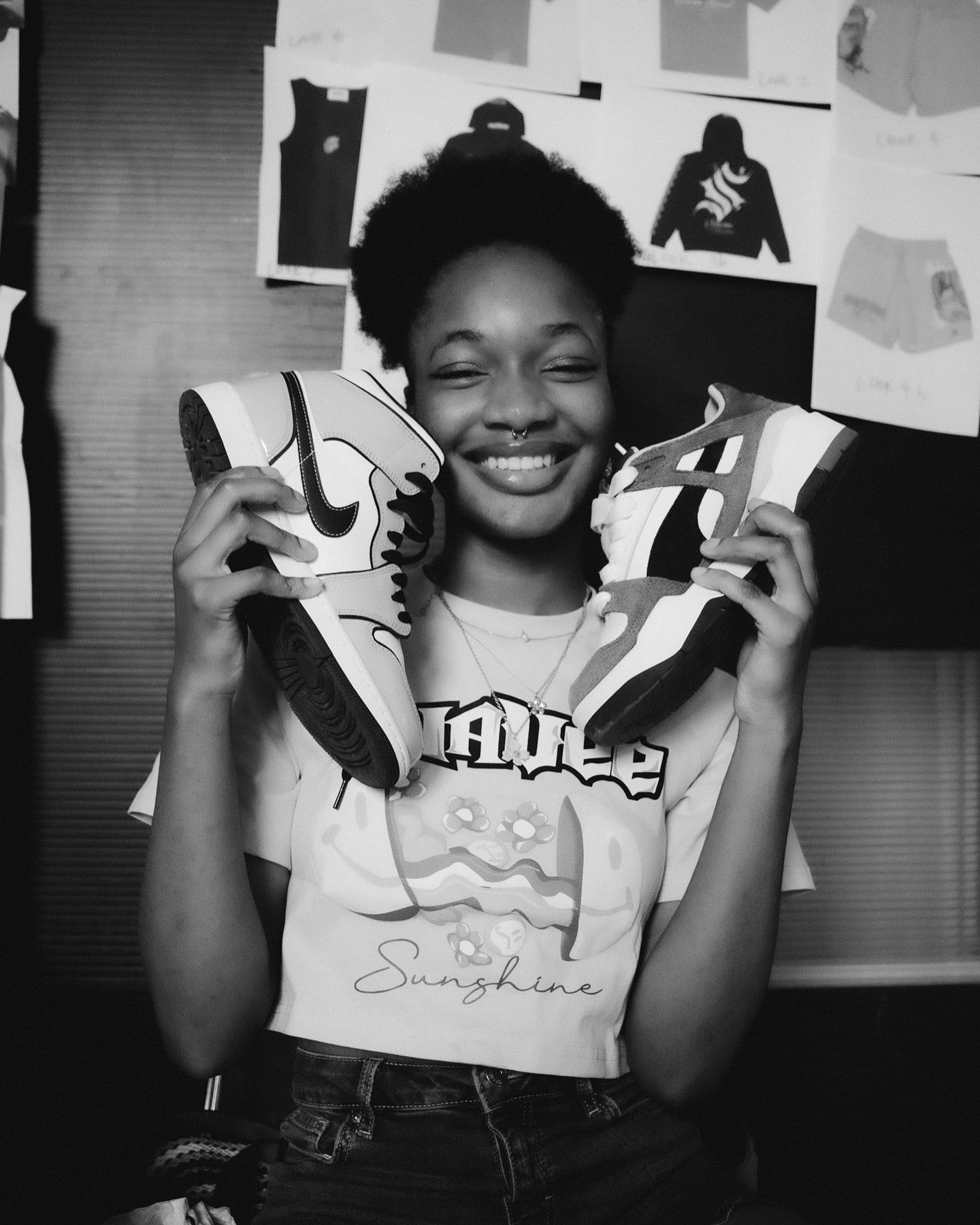 Smiling young woman holding Nike sneakers in black and white photo, wearing Sunshine graphic tee.