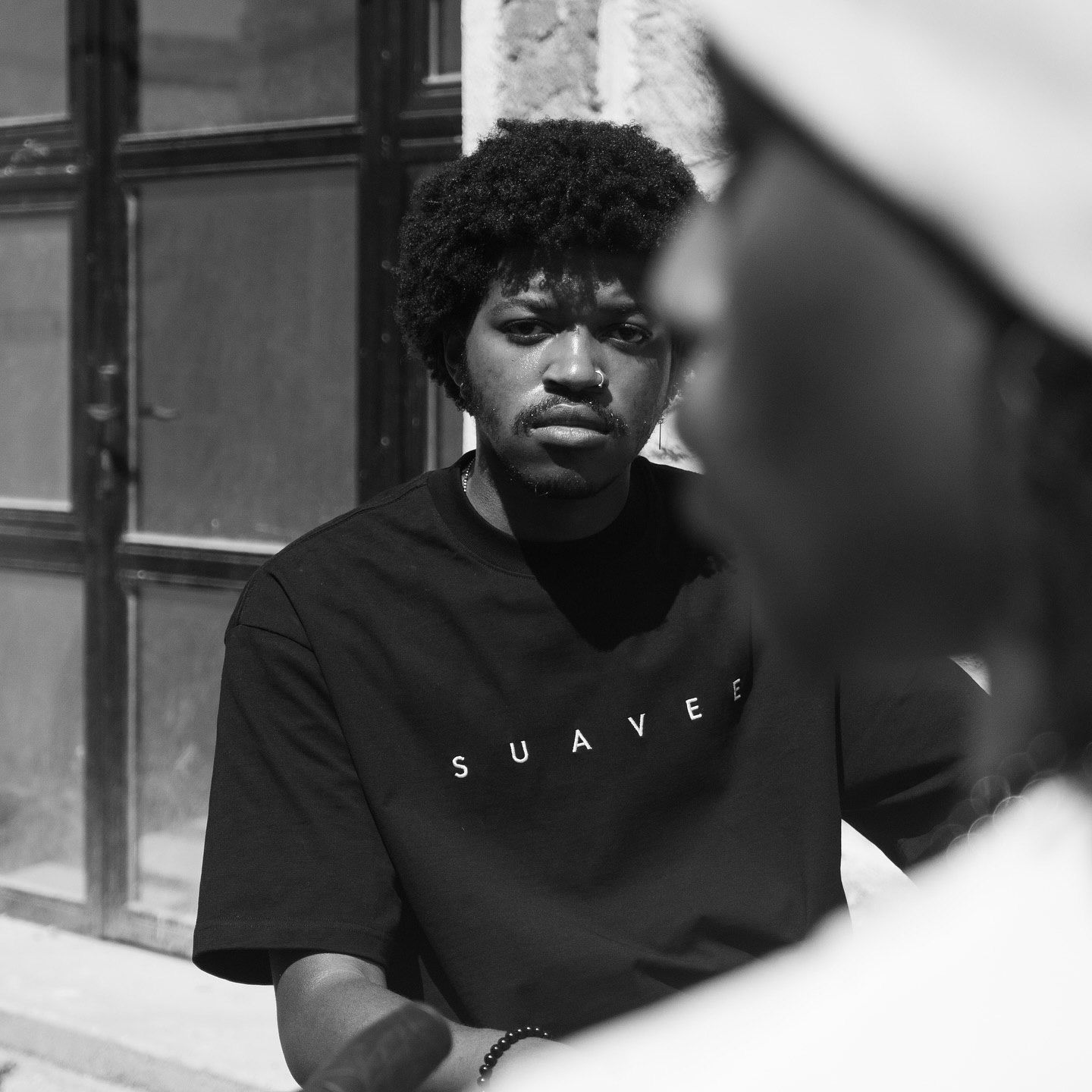 Young man wearing a black Suave t-shirt poses outdoors in a black and white street style portrait photo.