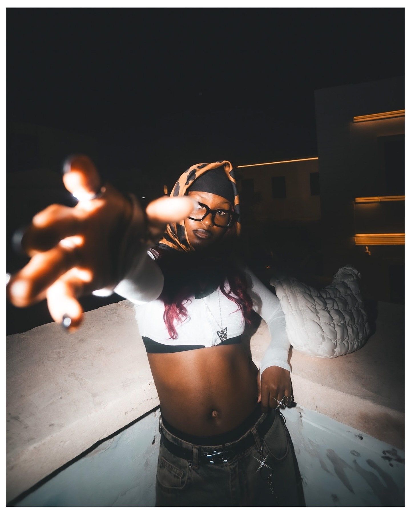Woman in white crop top reaches toward camera in dramatic nighttime outdoor photo.