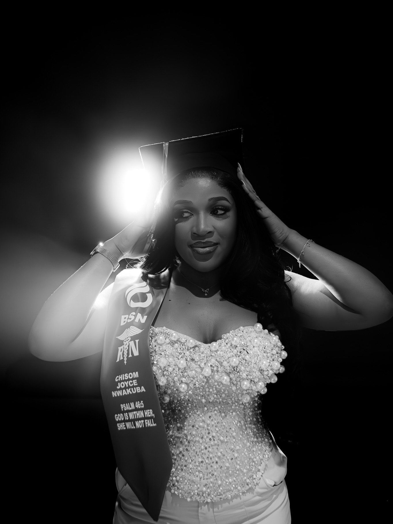 Black and white photo of woman in BSN RN nursing graduation attire under spotlight.
