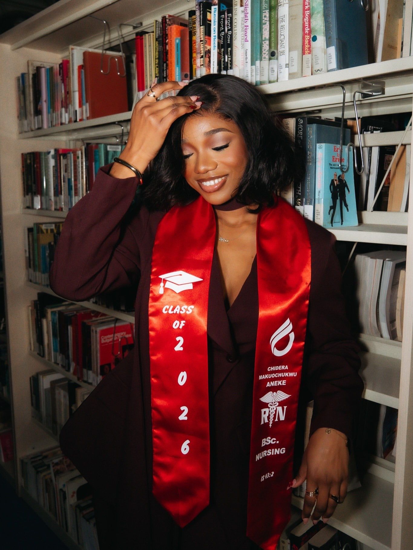 Smiling Black woman wearing Class of 2026 nursing graduation stole poses in library.