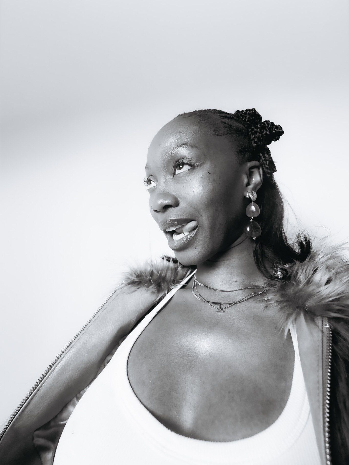 Close-up black and white portrait of young Black woman in white top with fur jacket looking sideways.