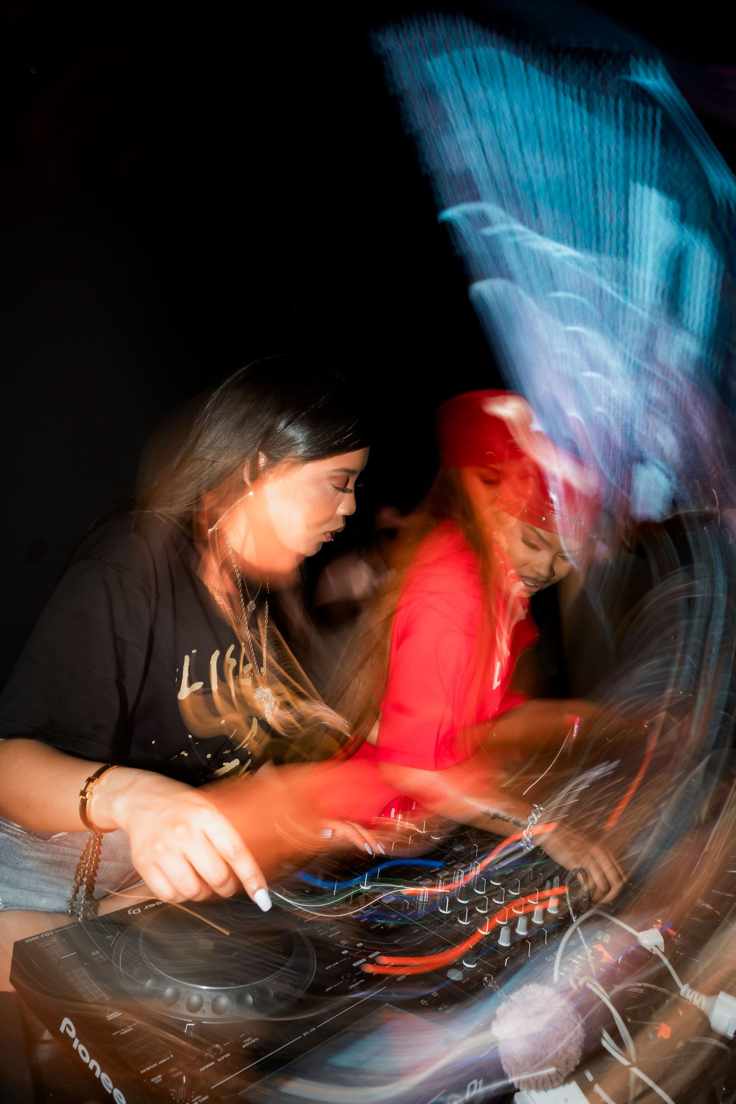 Two DJs performing at a nightclub with motion blur effects on Pioneer equipment in dynamic lighting.