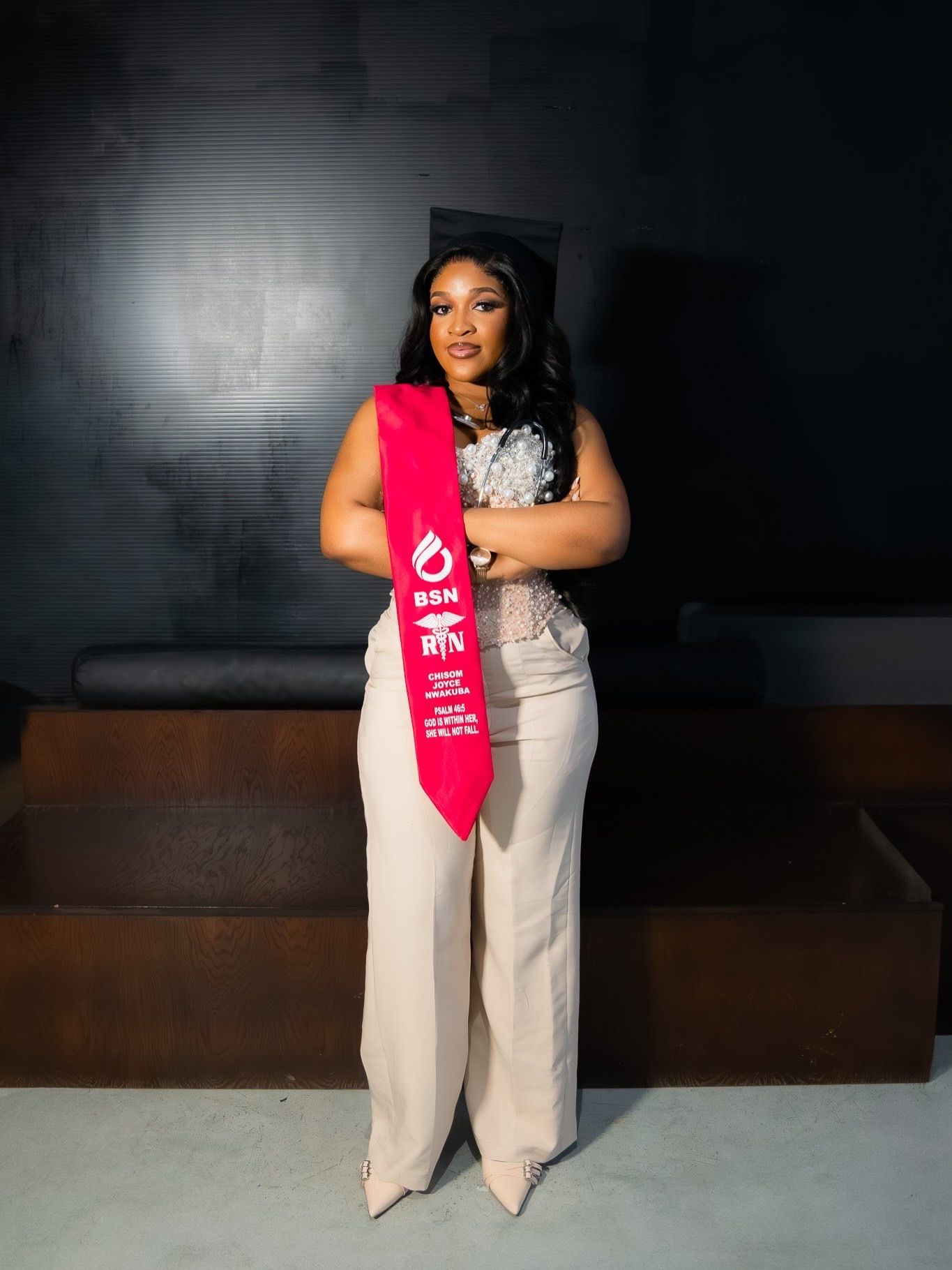 Young woman in BSN RN red nursing graduation sash standing in white outfit.