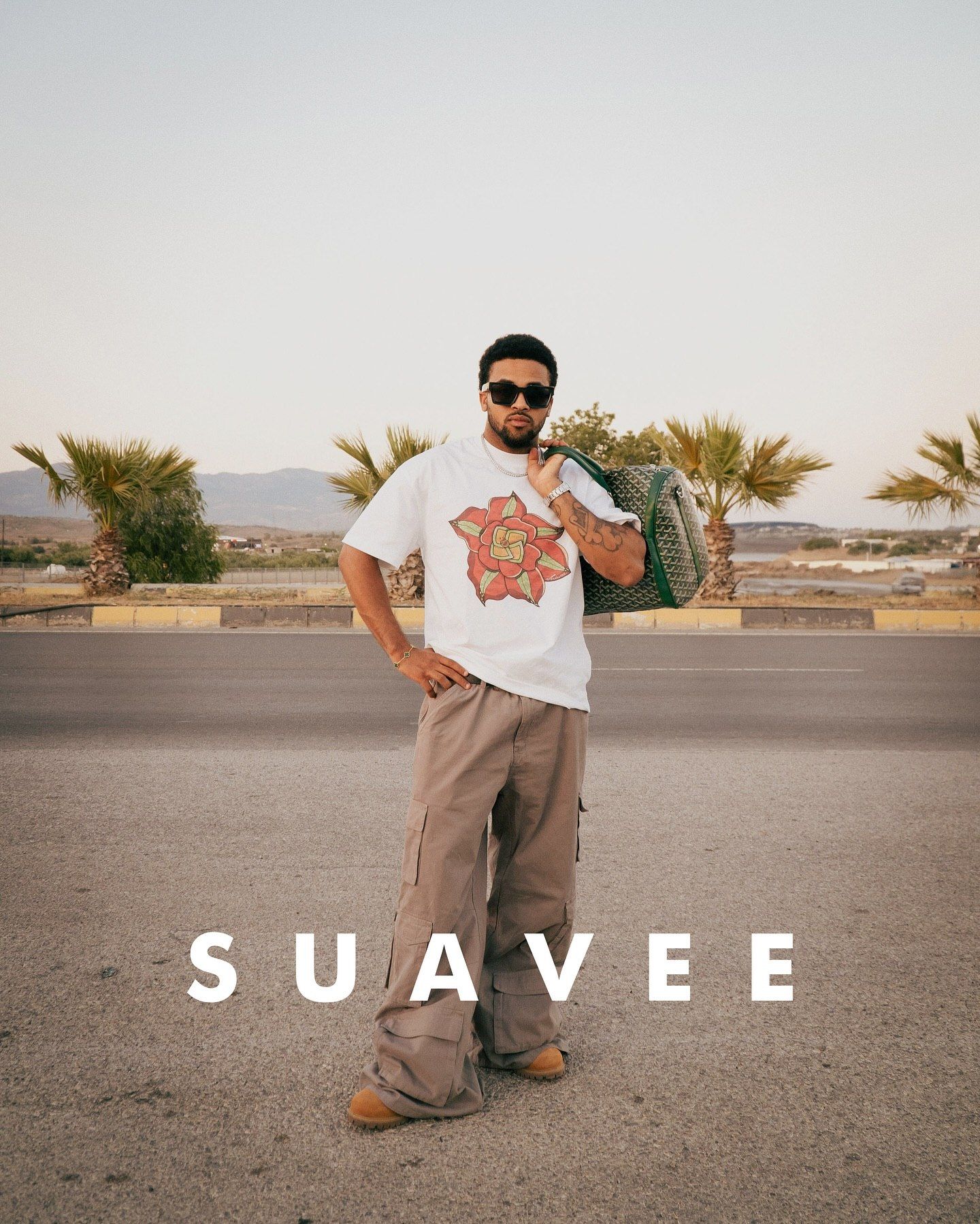 Man in white graphic tee, cargo pants, and sunglasses posing outdoors with SUAVEE branding.