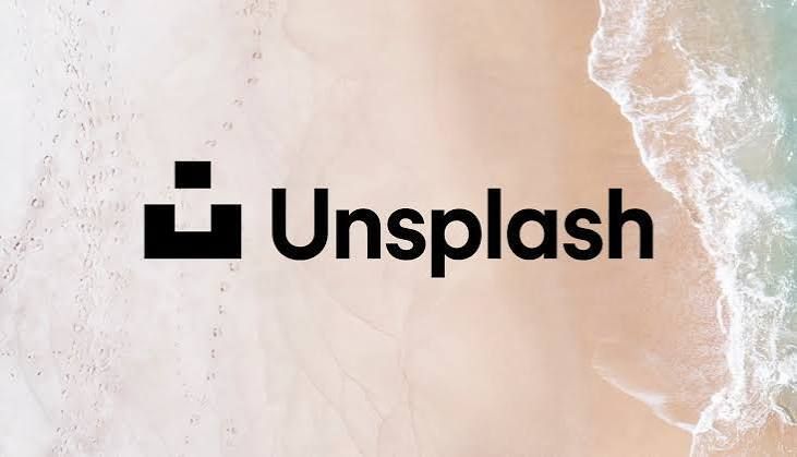 Unsplash logo displayed over an aerial view of ocean waves gently washing onto a sandy beach.