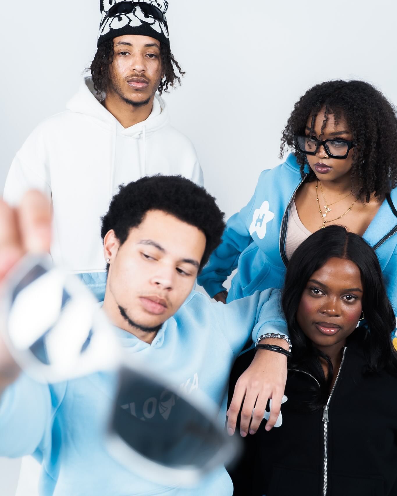 Four stylish young adults pose together in a trendy photoshoot wearing blue and white streetwear outfits.