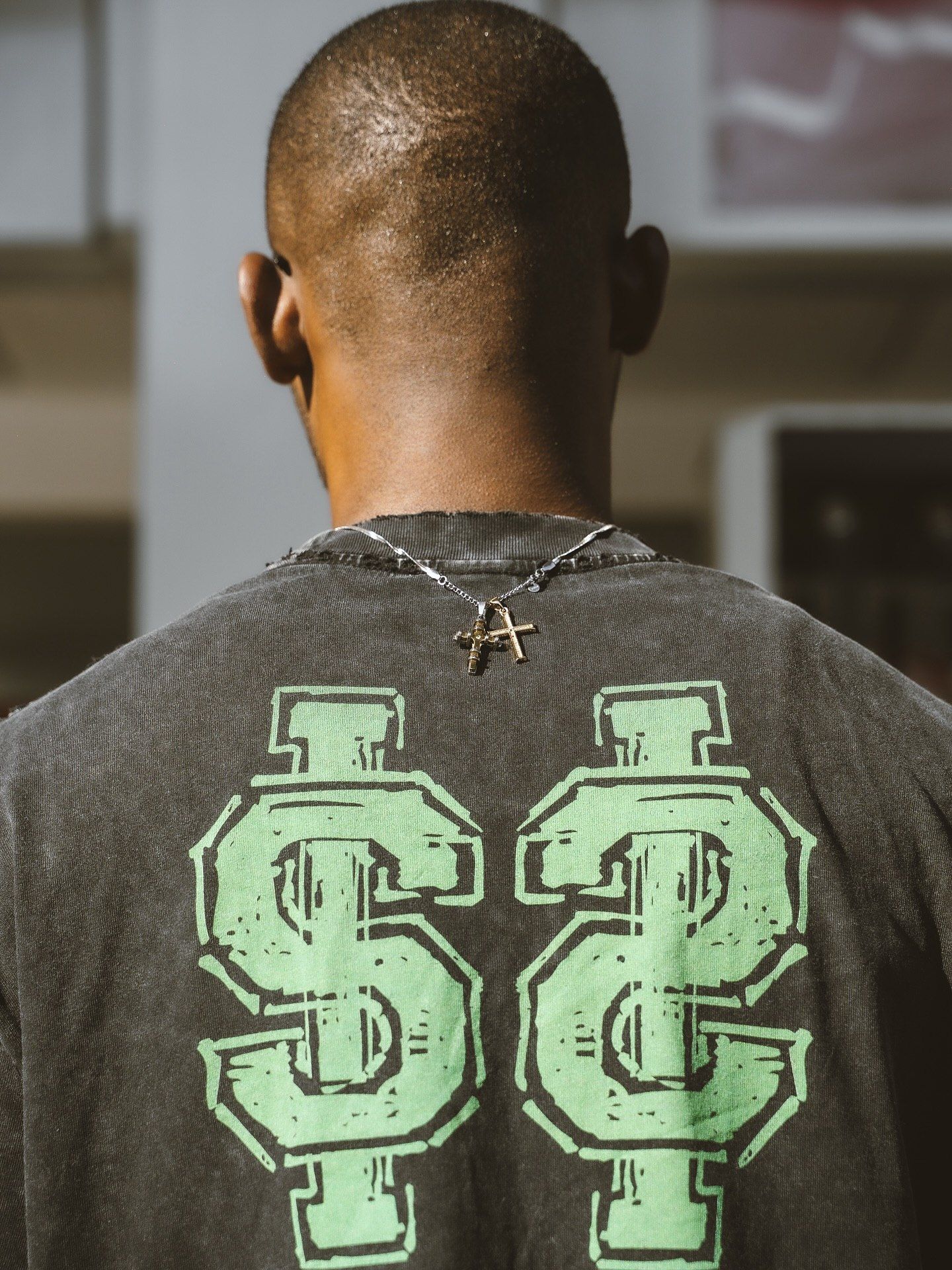 Man from behind wearing dark graphic tee with green SC logo and cross necklace.