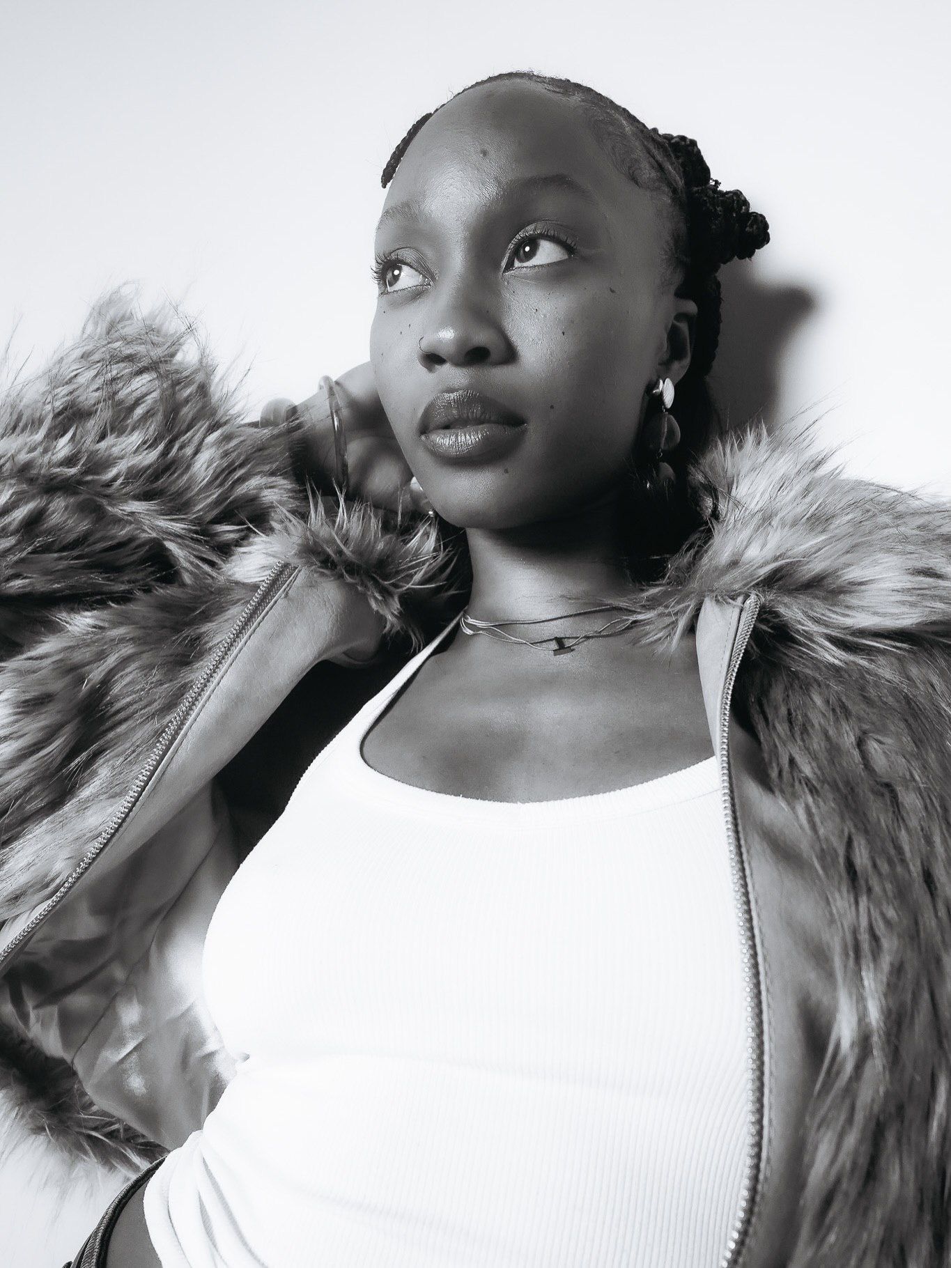 Black and white portrait of a woman in a fur jacket and white top looking upward confidently.