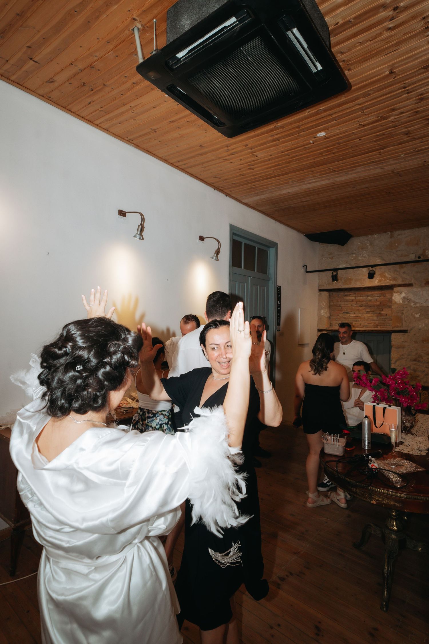 Bride in white dress high-fiving a guest in black at a wedding reception indoors.