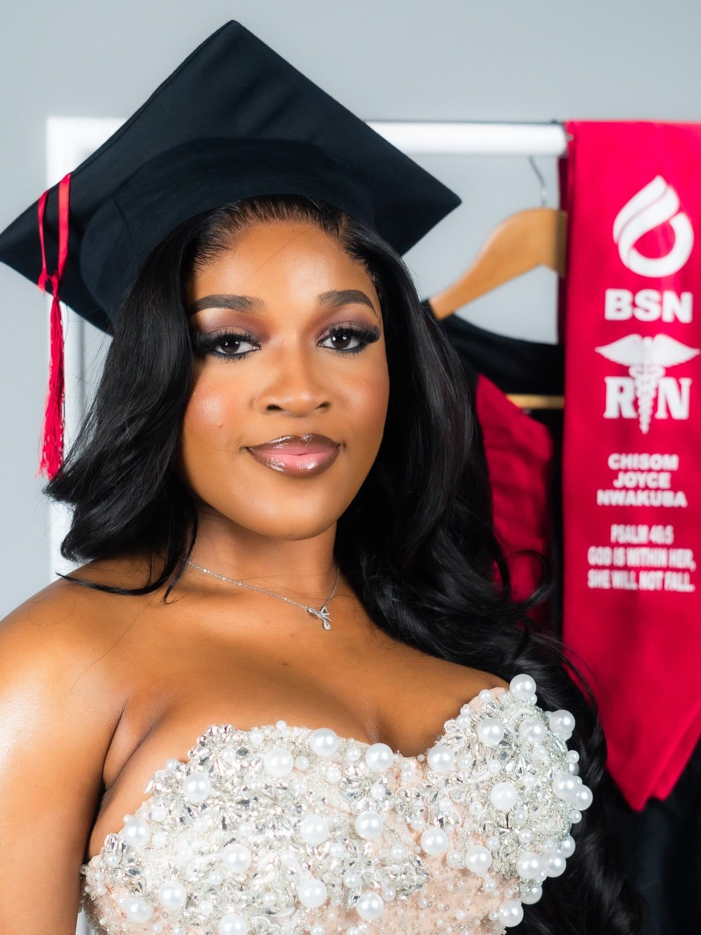 Woman in strapless gown wearing graduation cap with BSN RN sash on rack behind.
