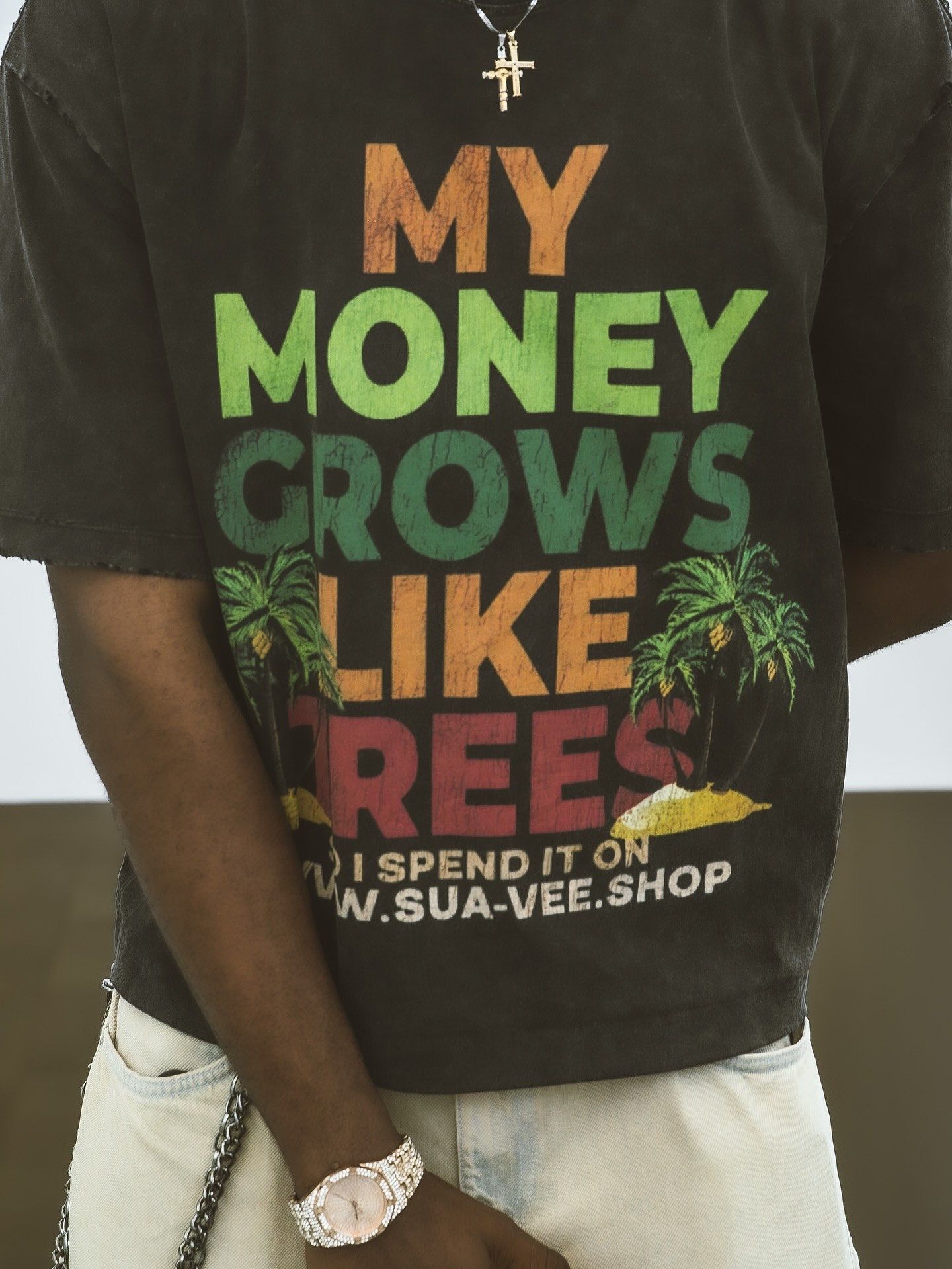 Dark graphic tee with colorful MY MONEY GROWS LIKE TREES print and sua-vee.shop branding, worn with white jeans.