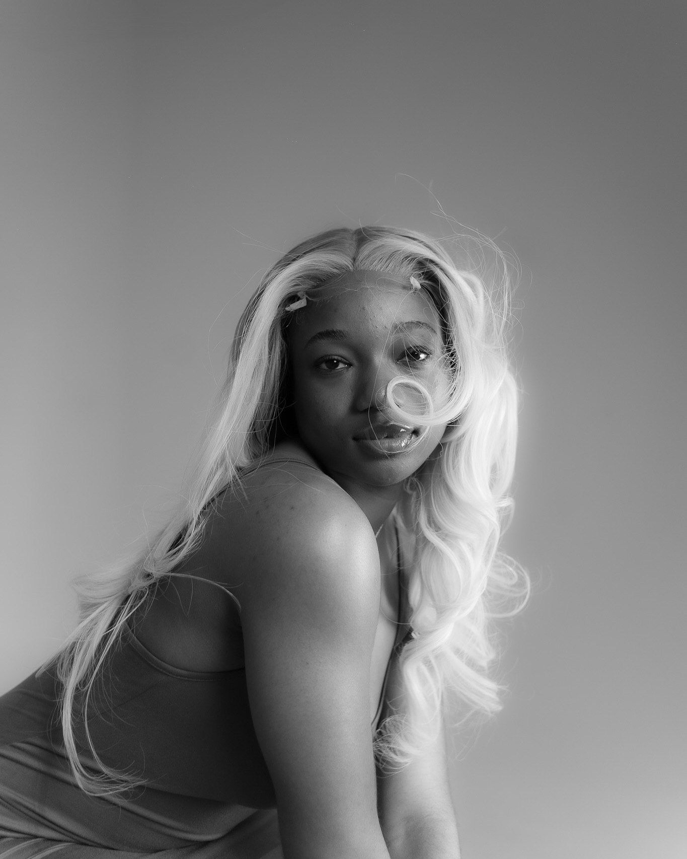 Black and white portrait of a woman with long blonde hair blowing in the wind against gray background.