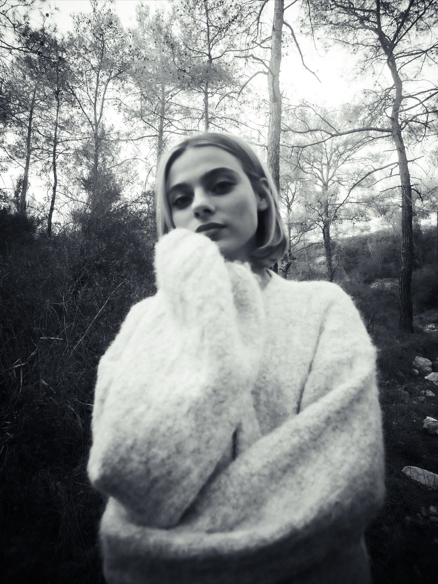Black and white portrait of a young woman in a fluffy white sweater posing thoughtfully in a forest setting.