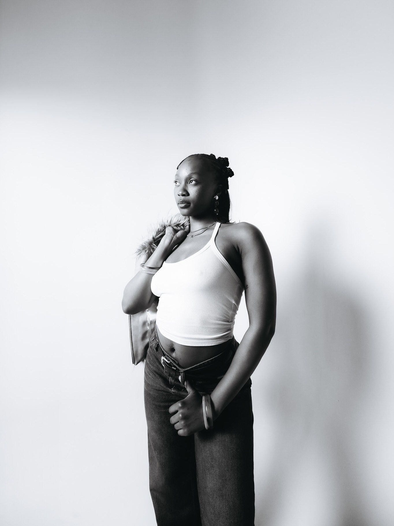 Black woman in white crop top and jeans poses confidently against white background in black and white photo.