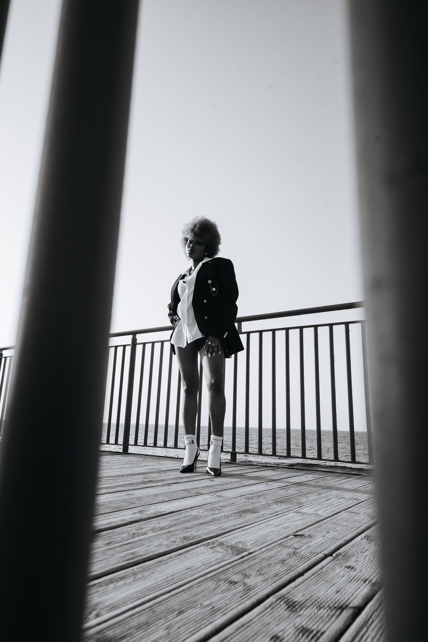 Black and white photo of woman in blazer standing on wooden pier overlooking the ocean.