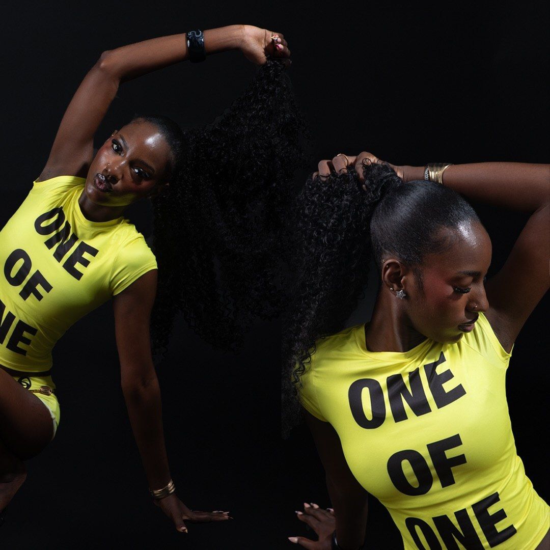 Two women in matching neon yellow ONE OF ONE shirts strike dynamic poses against a dark background.