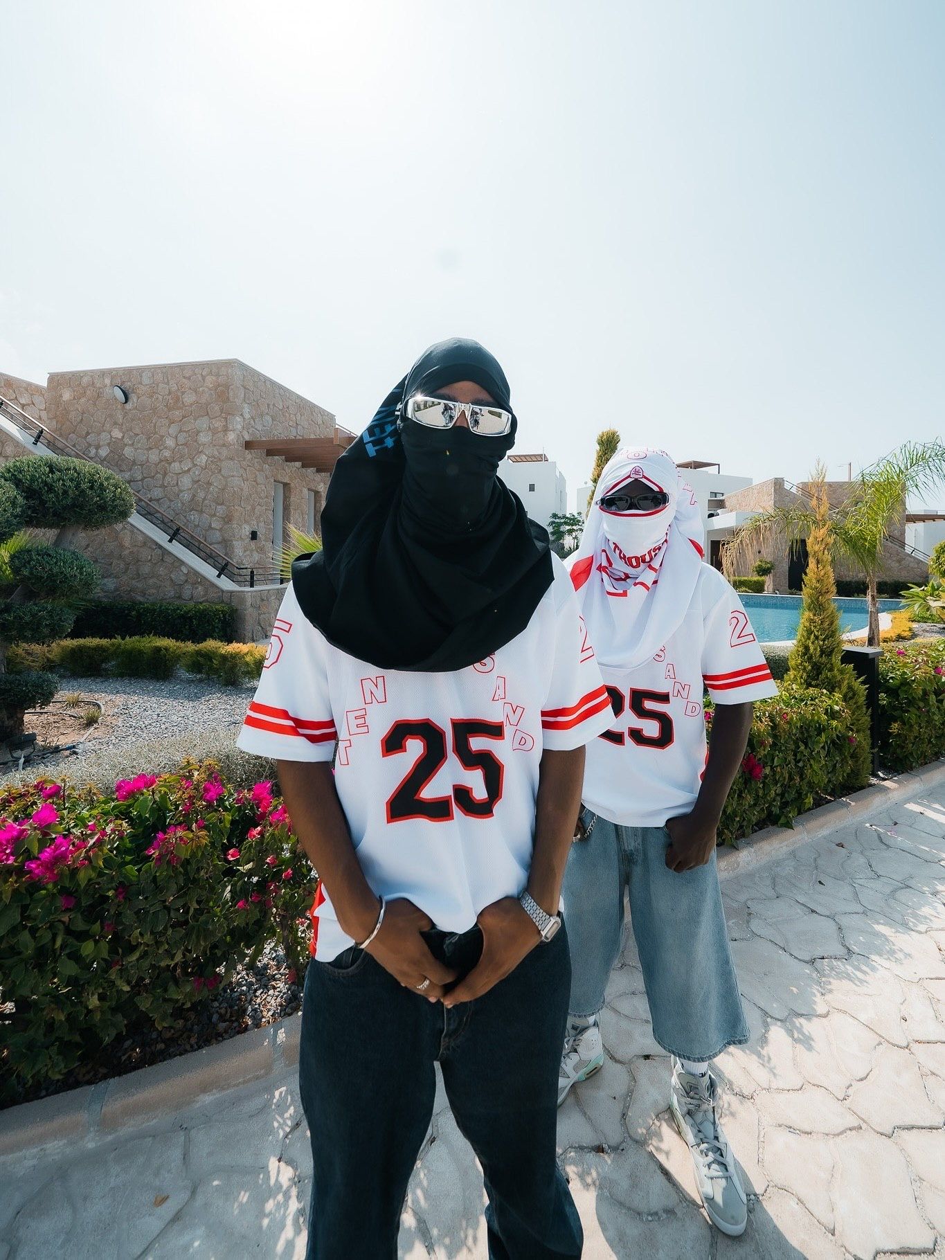 Two people wearing matching white number 25 jerseys pose outdoors near a pool, one in a black hijab and face covering.