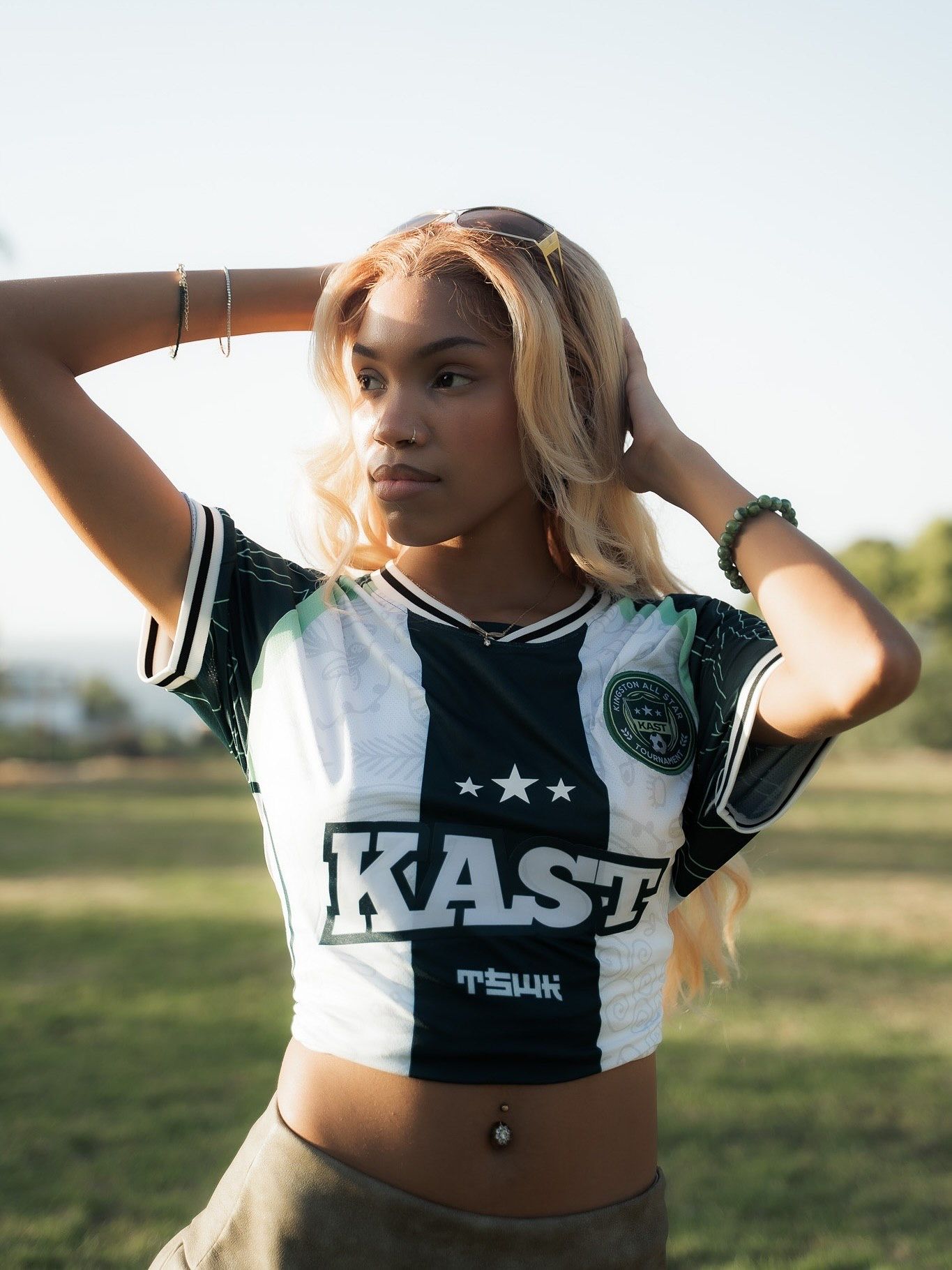 Young woman in a KAST crop soccer jersey with blonde hair poses outdoors in natural light.