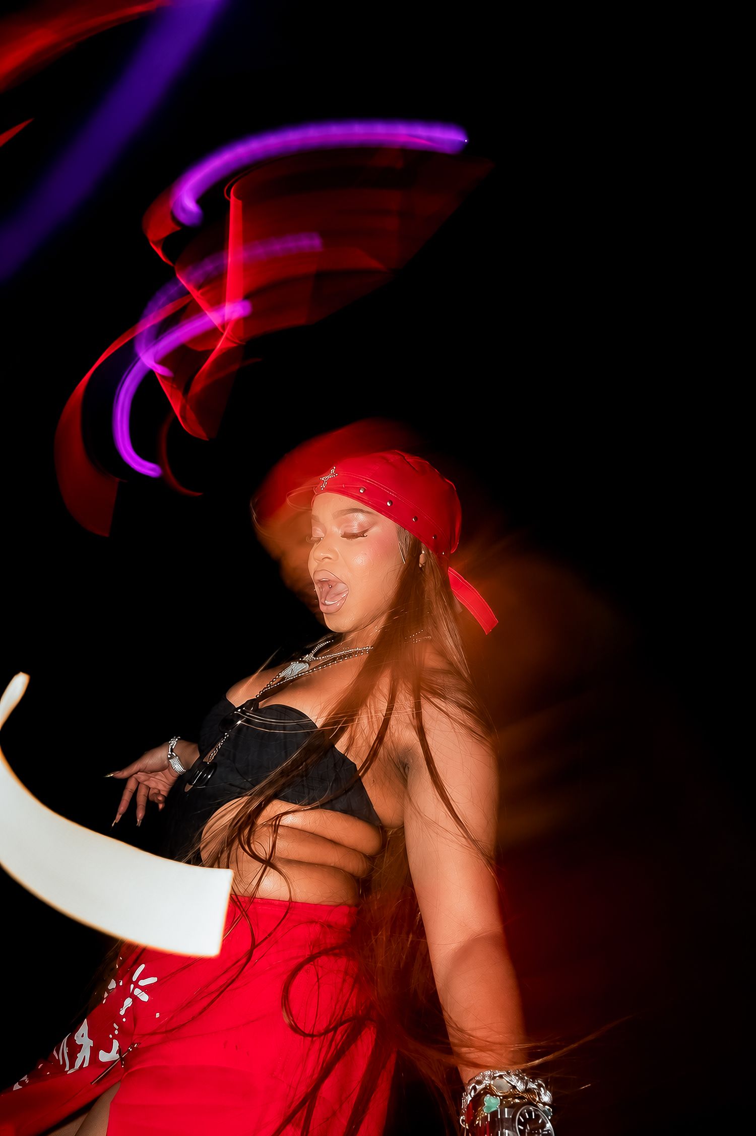 Woman in red bandana and outfit dancing energetically with colorful light trails in dark nightclub setting.