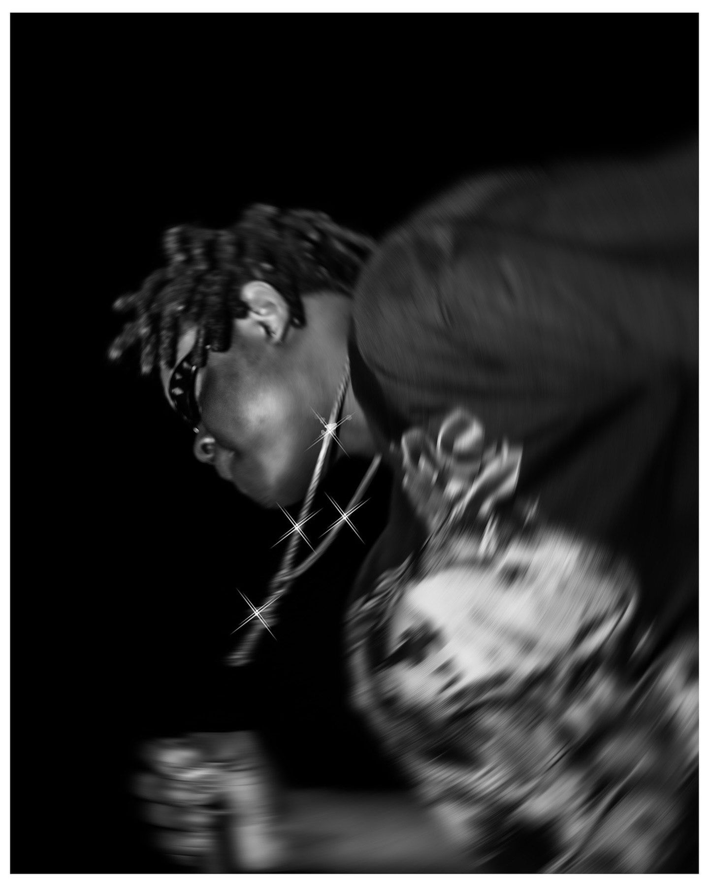Black and white photo of a performer with dreadlocks and chain necklace leaning forward on stage.