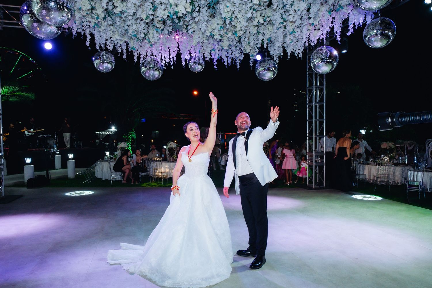 Bride and groom dancing joyfully under disco balls and floral ceiling decorations at an elegant outdoor wedding reception.