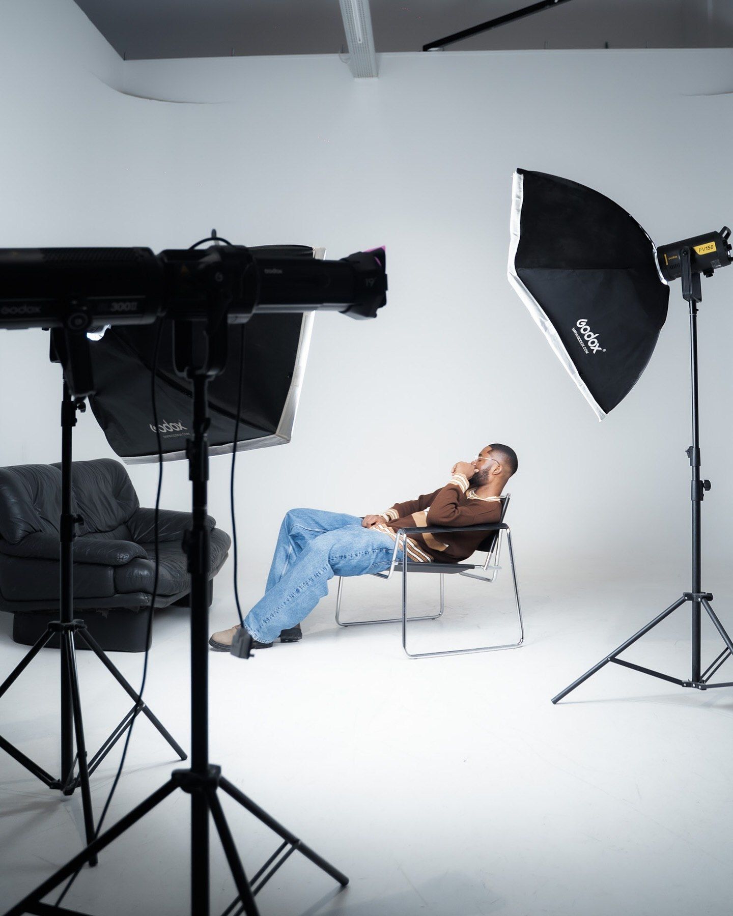 Photographer's studio setup with softbox lights surrounding a person relaxing in a chair.