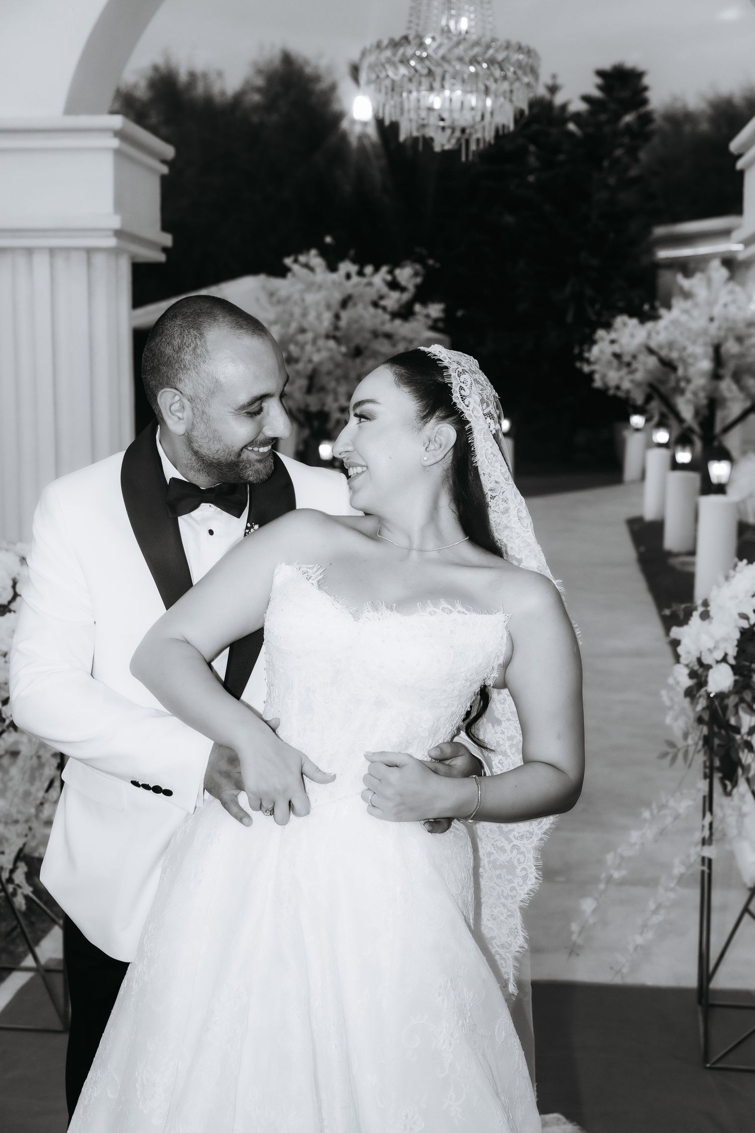 Black and white photo of a smiling bride and groom in wedding attire at an elegant outdoor ceremony venue.