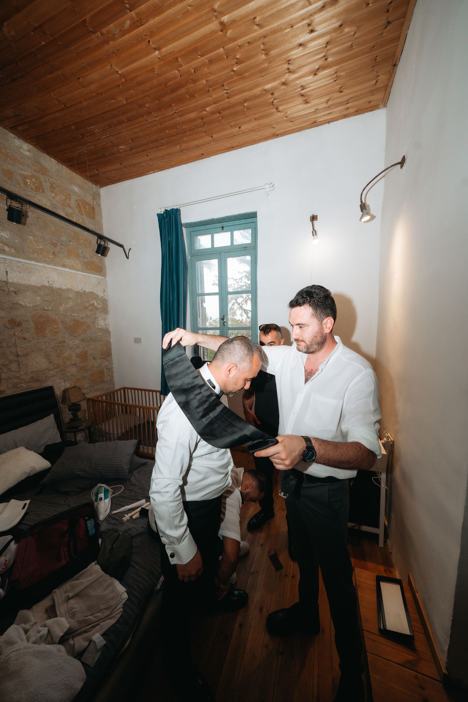 Three men getting ready in a rustic room with wooden ceiling, stone walls, and hardwood floors.