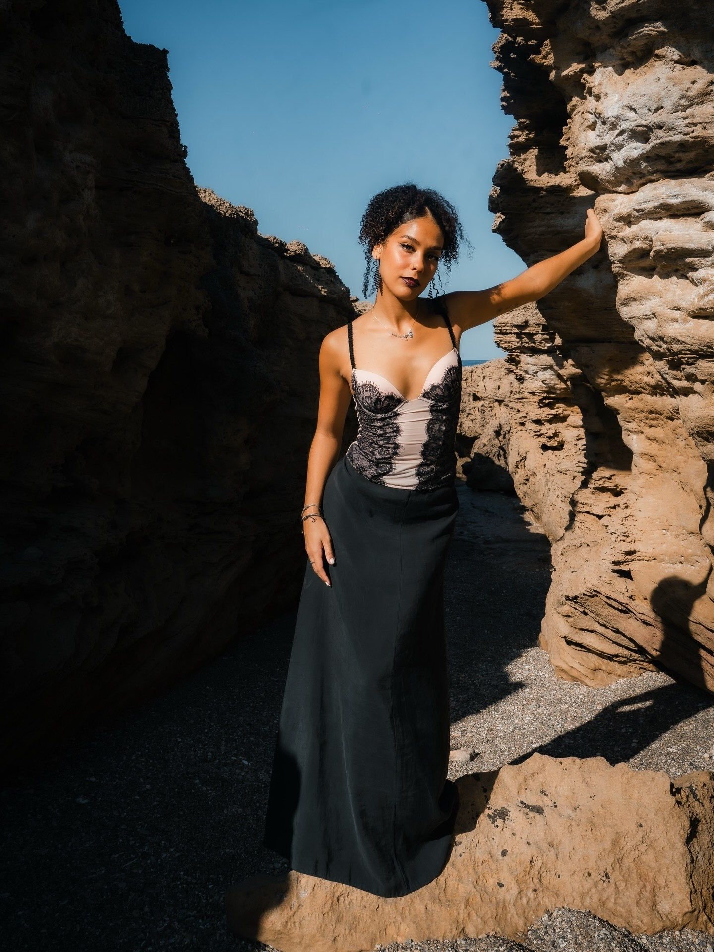Woman in black gown posing among sandy rock formations on a sunny day.