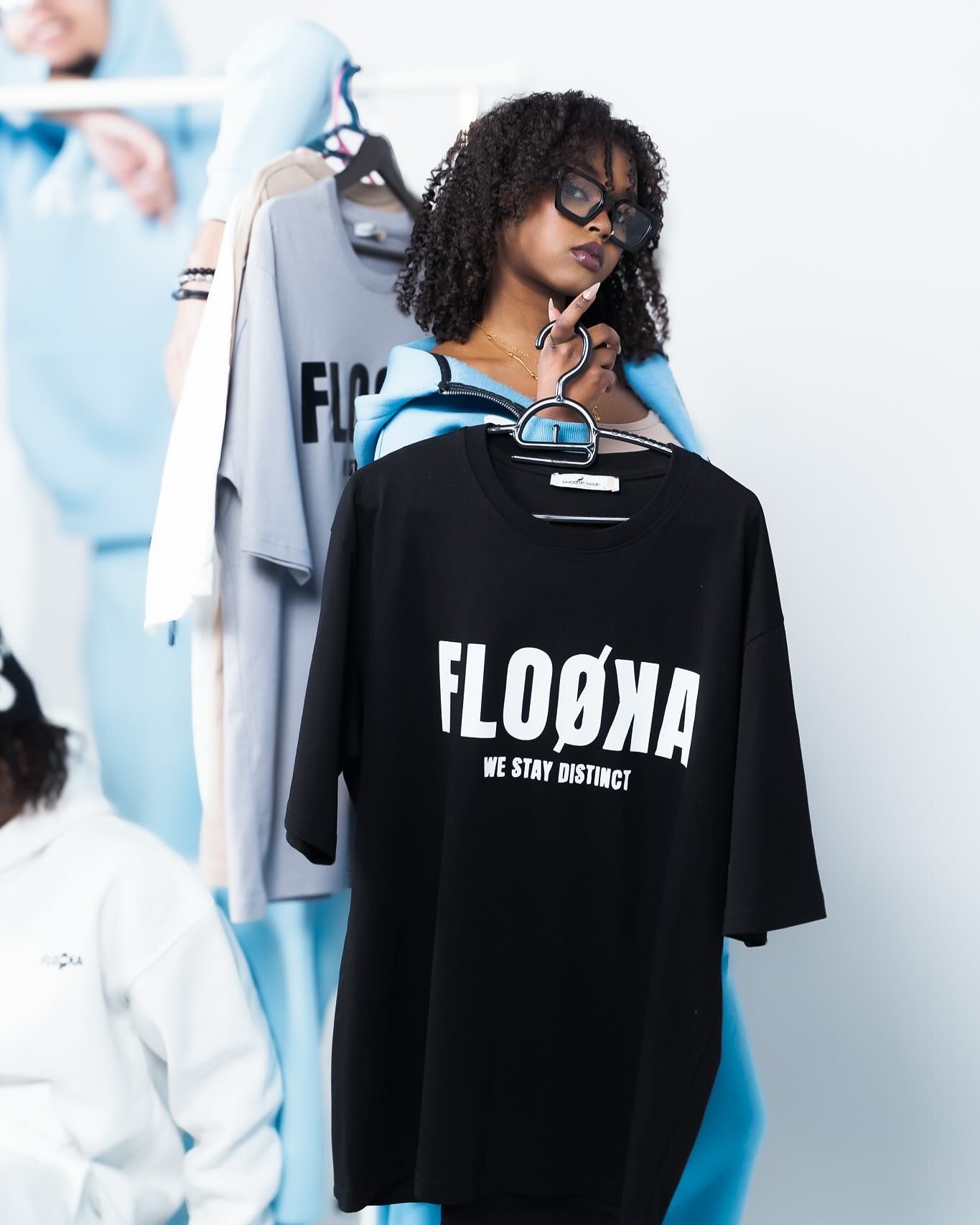 Woman holding a black FLOØKA 'We Stay Distinct' oversized t-shirt in a clothing store.